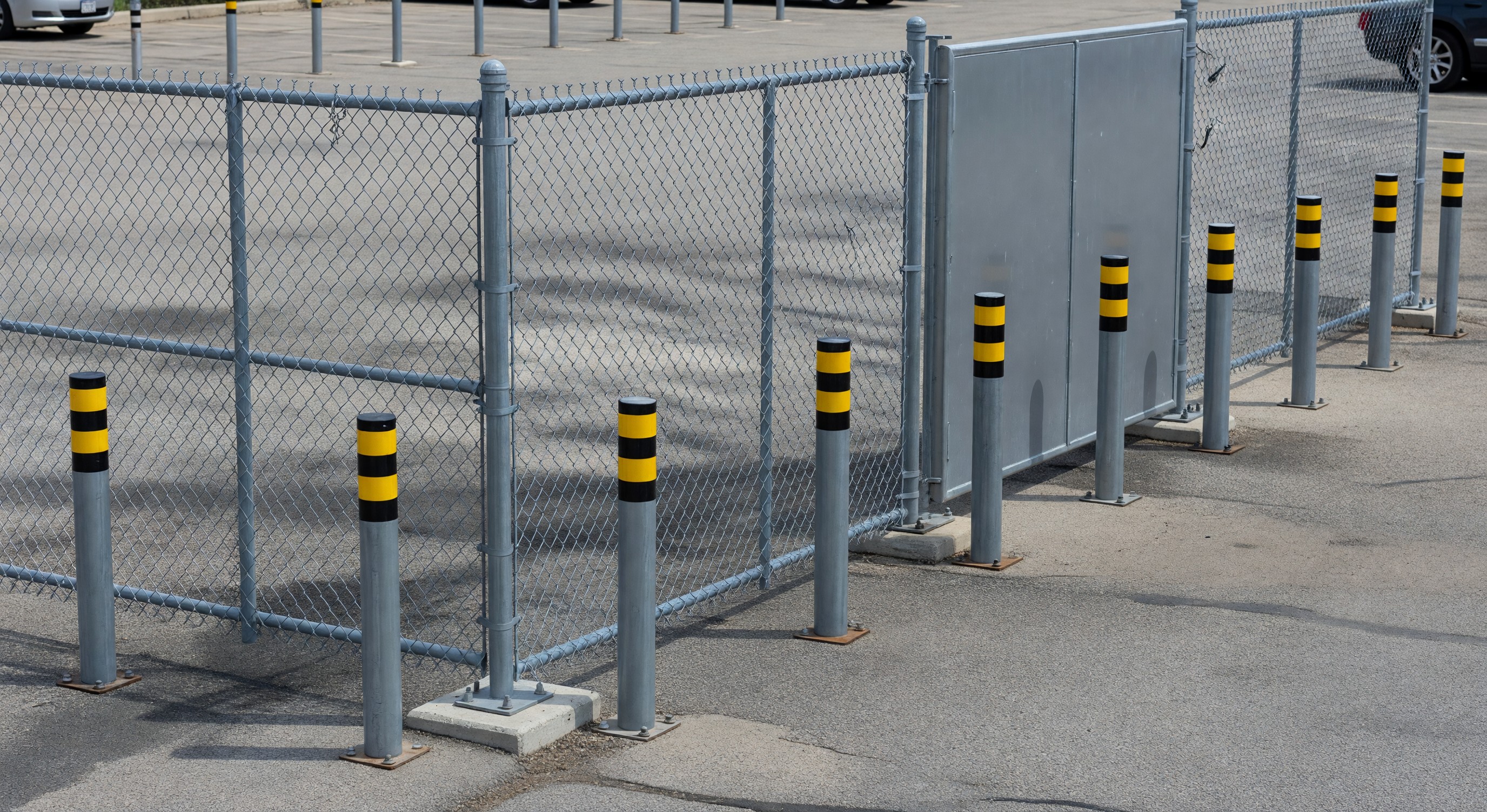 Parking lot perimeter with security fencing, vehicle gate, and bollard installations