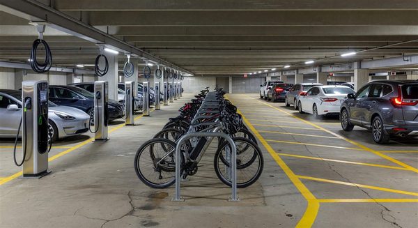 Parking garage ground floor integrating EV charging stations, bike parking, and rideshare pickup zone