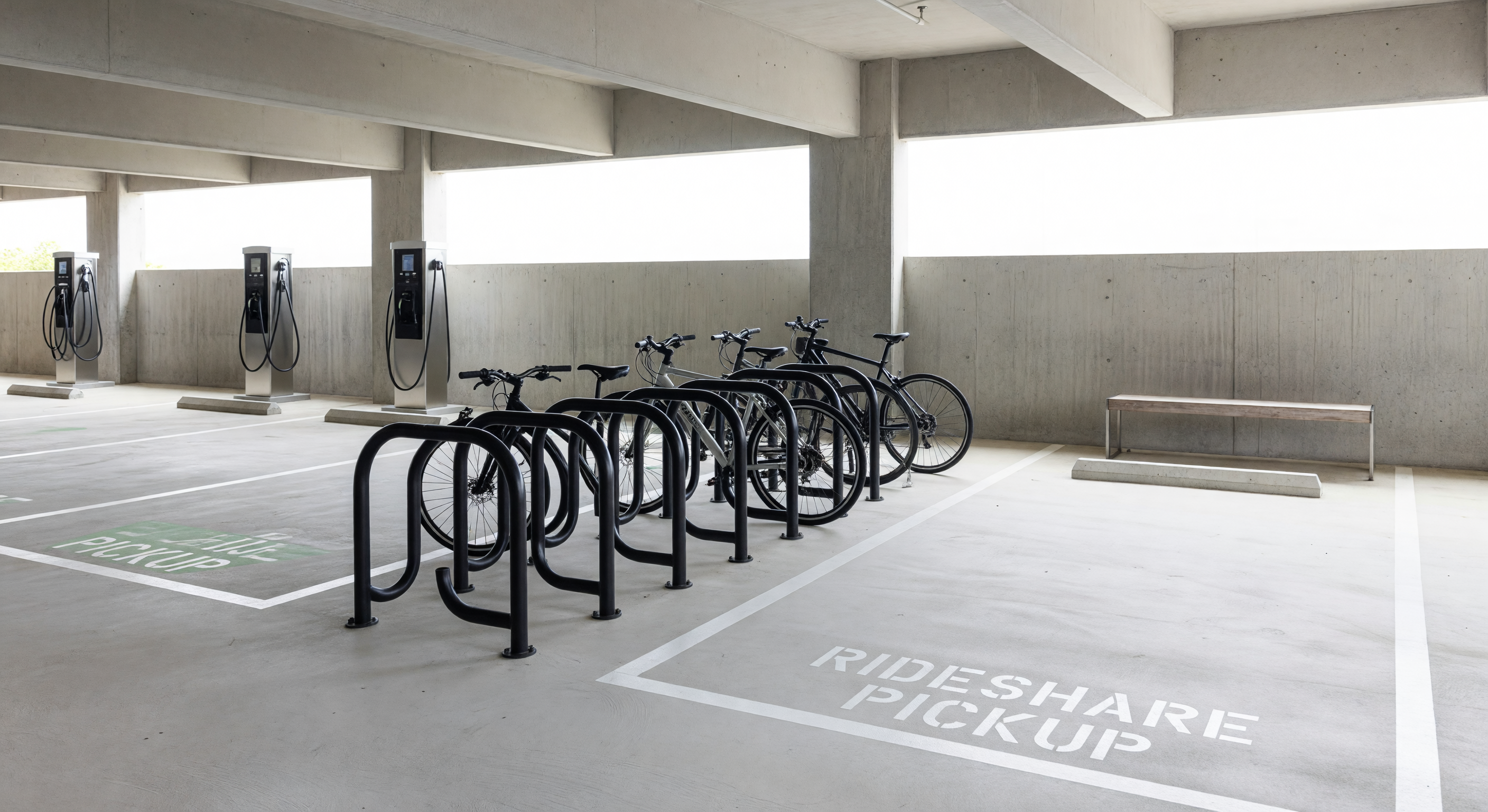 Parking garage ground floor integrating EV charging stations, bike parking, and rideshare pickup zone