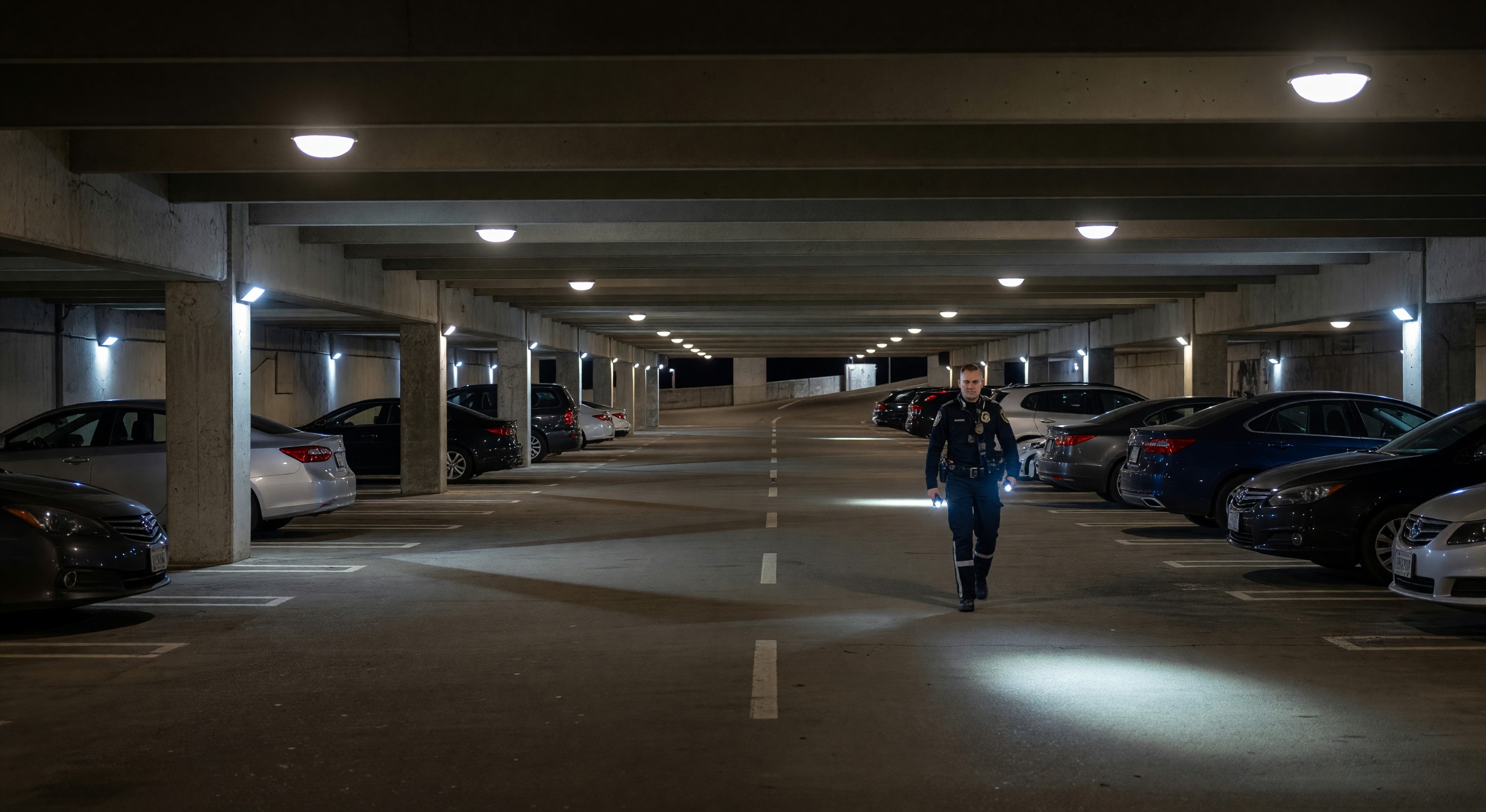 Parking facility at night with security lighting and a security officer making rounds