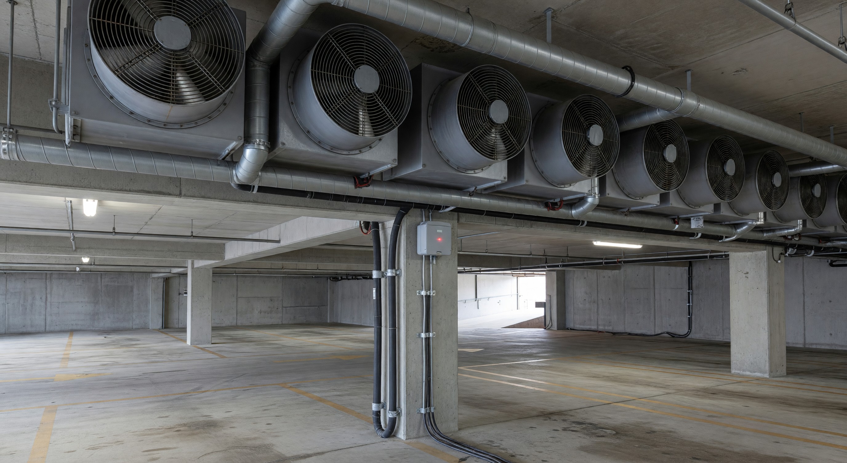 Parking structure interior showing ventilation fans and carbon monoxide sensor installation