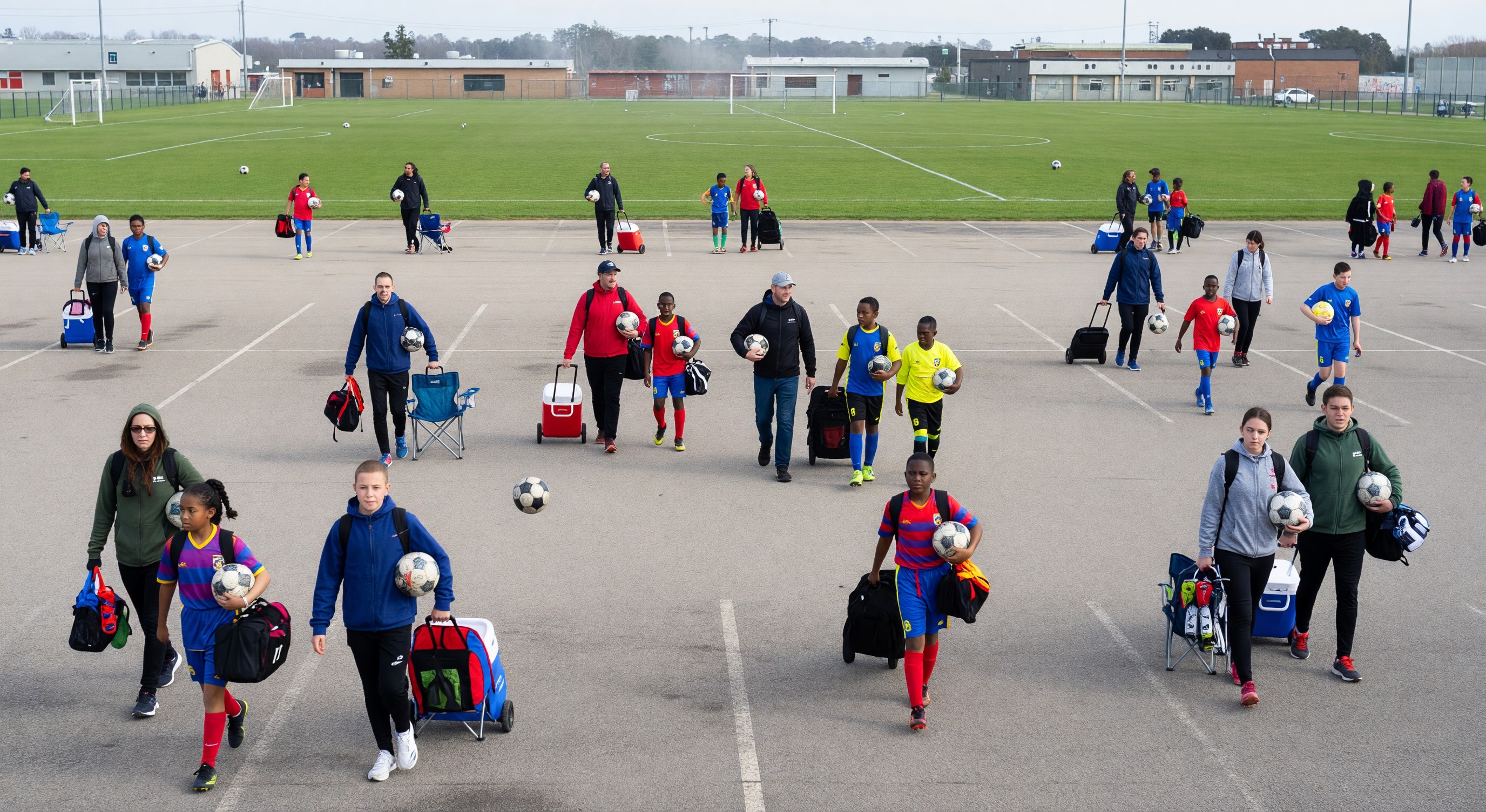 Youth soccer tournament parking lot at multi-field sports complex with families walking to fields with equipment