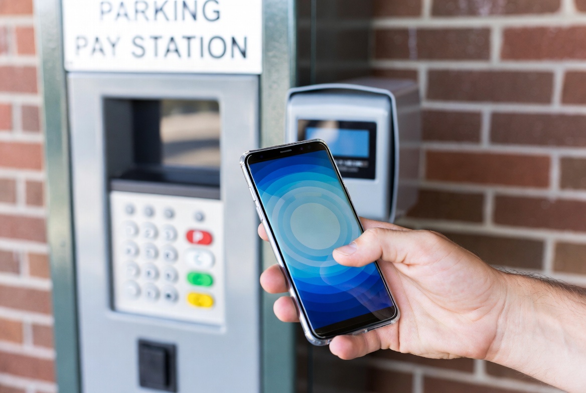 Smartphone being tapped against contactless payment terminal at parking station