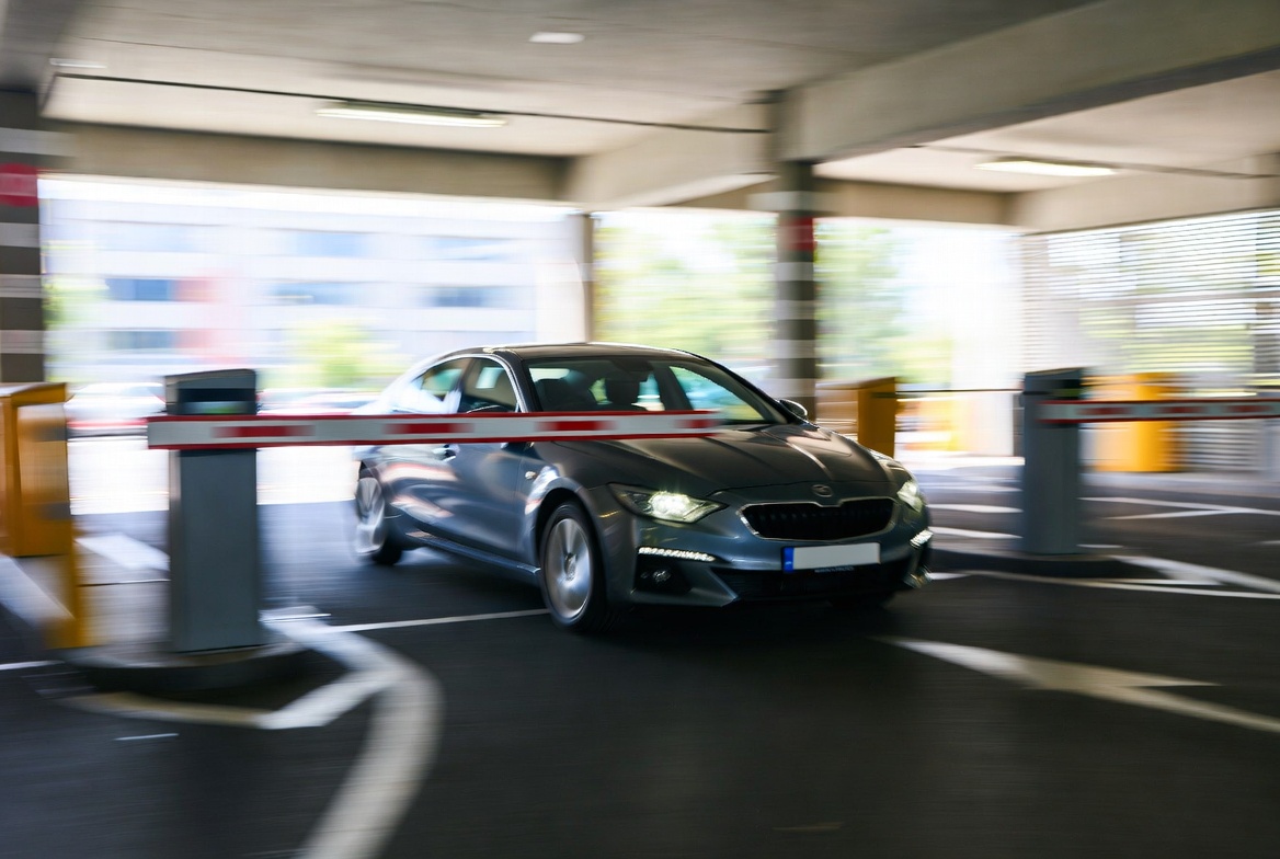 Car driving through parking entrance with barrier gate lifting automatically